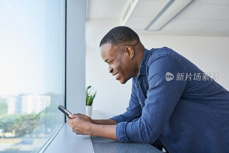 快乐的非裔美国商人在办公室使用电话。微笑的男人在办公室看智能手机