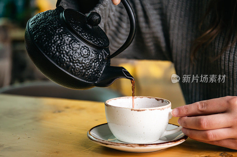 咖啡馆里的女人用黑色铸铁茶壶倒茶。