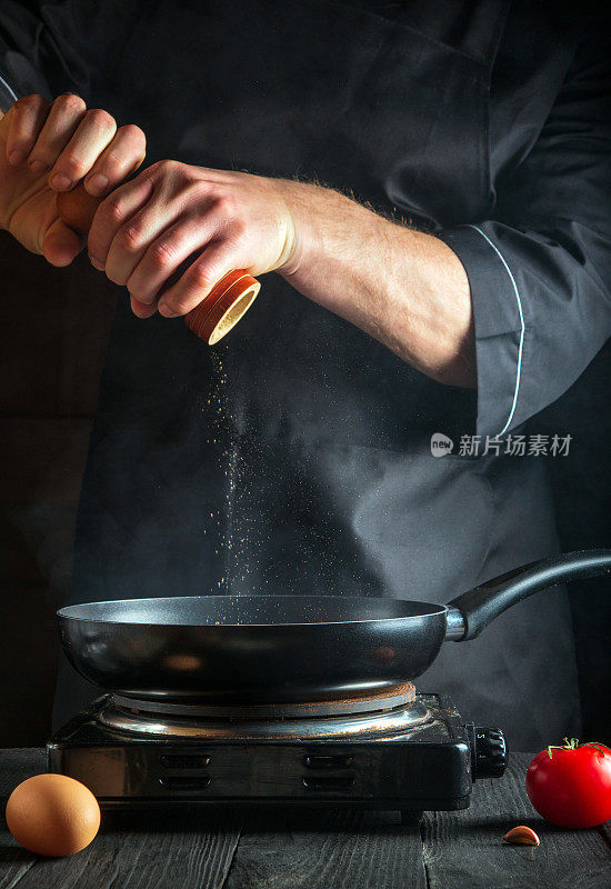 厨师在锅里煮鸡蛋时加了胡椒粉。在老式厨房桌子上的工作环境。垂直的图像