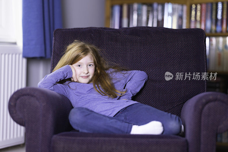 红头发的年轻女孩舒适地蜷缩在扶手椅上