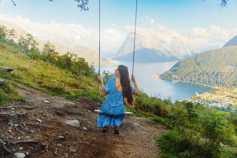 一名身穿蓝色连衣裙的女子在挪威夏季峡湾的美景中摇摆