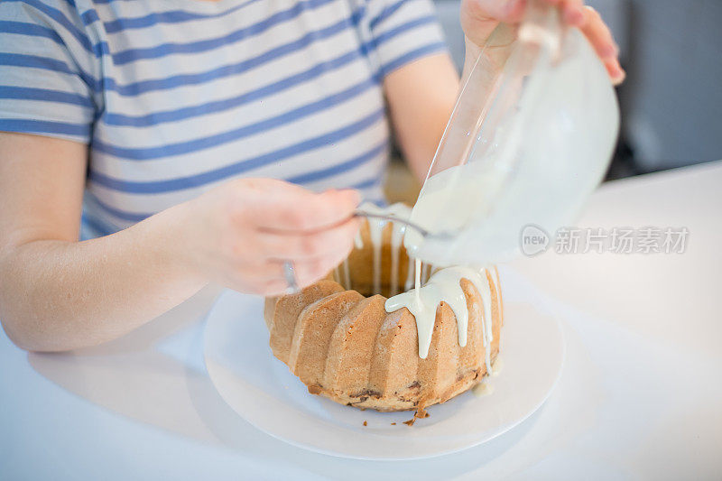 年轻女子正在装饰库格霍夫蛋糕，并把融化的白巧克力倒在上面