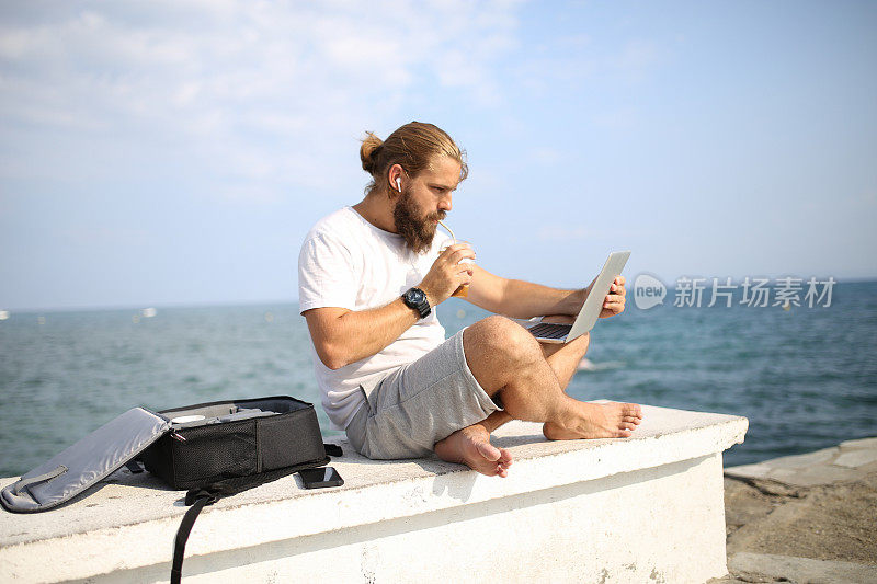 一名男子一边在海滩上放松，一边在笔记本电脑上阅读电子邮件