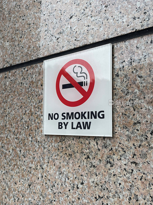 矩形图像，高度抛光的石墙上的法律禁止吸烟标志，红色边框圆圈，白色背景和黑色香烟，红色对角线穿过烟雾符号，重点放在前景上