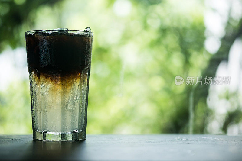 玻璃杯中的冰美式咖啡，在自然背景下呈现出两层黑咖啡和水