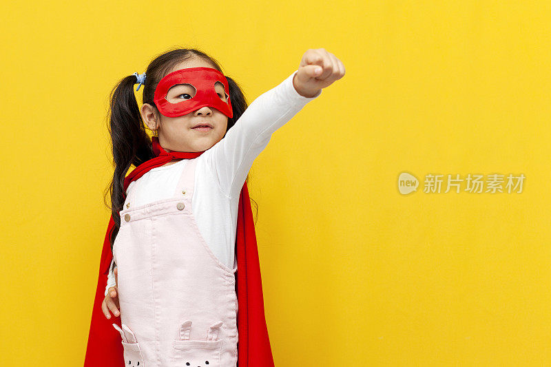穿着超人服装和面具的亚洲小女孩伸出手飞起来，穿着超级英雄斗篷的韩国孩子