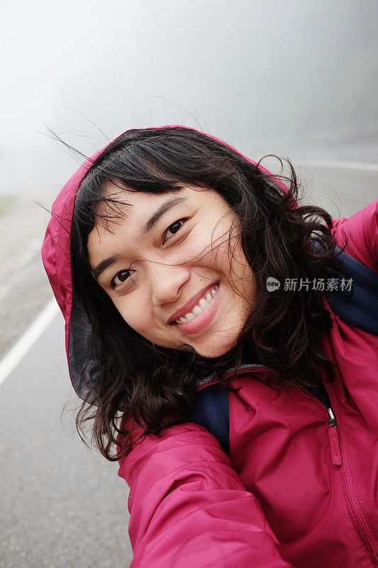 微笑的年轻亚洲女子在热带雨林中旅行和自拍，在泰国度假的路上下着雨和雾