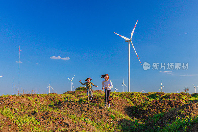 女孩们喜欢在户外跑步，在农村的绿色山丘上玩风力涡轮机