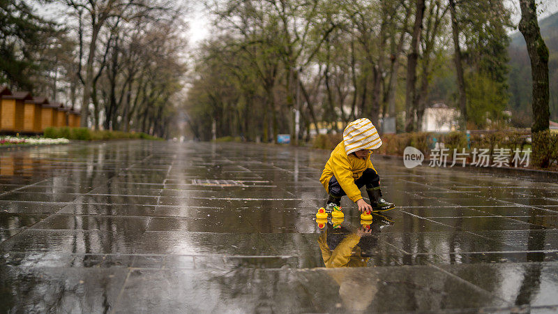 漂亮有趣的金发小孩带着橡皮鸭，在水坑里跳跃，在雨中玩耍