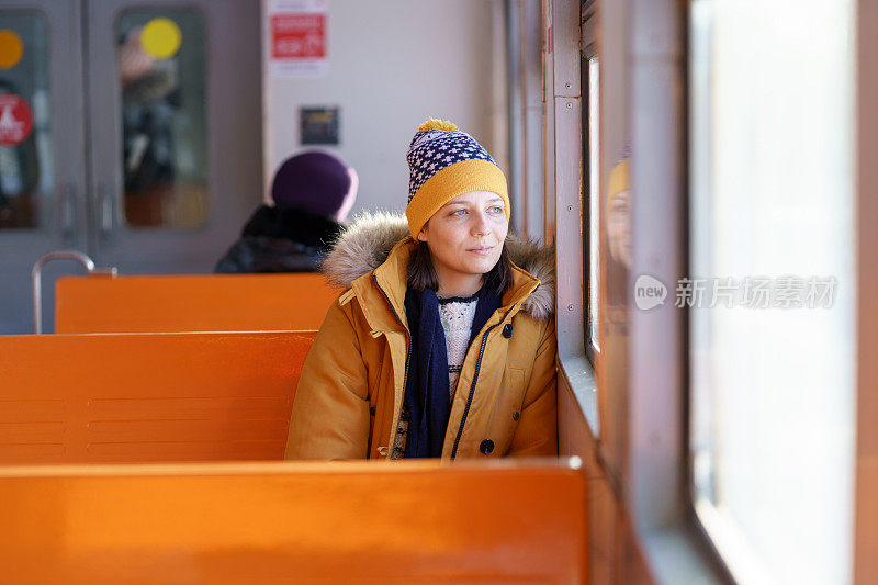 沉思的年轻欧洲妇女戴着帽子，在冬天乘火车旅行，一边沉思，一边望着窗外。