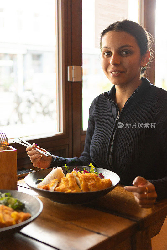 年轻女子在餐厅里吃着越南菜，配上蔬菜、鸡肉和咖喱酱米饭