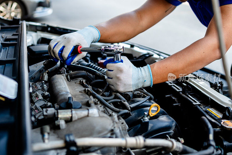 汽车修理工使用套筒扳手在车房内修理发动机，更换备件，检查汽车的里程，检查和维护服务的概念。