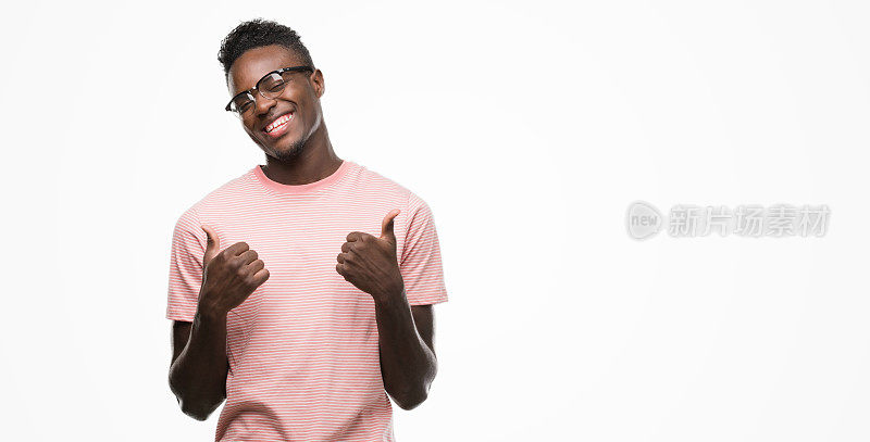 年轻的非洲裔美国人穿着粉色t恤成功标志做积极的手势，拇指向上微笑和快乐。带着愉悦的表情看着镜头，胜利者的姿态。