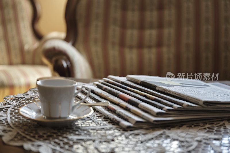 咖啡杯和几份报纸放在一个老式的白色绣花花边桌布上