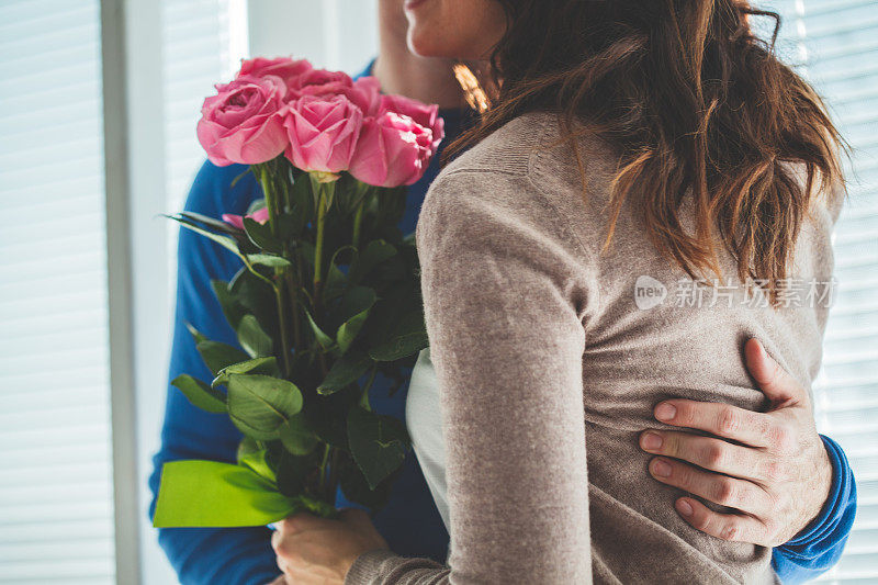 男子将一束粉色玫瑰送给妻子后，两人拥抱在一起