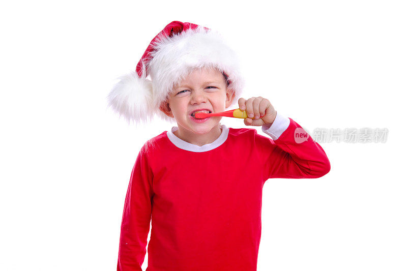 圣诞牙科。快乐的金发男孩男孩在红色的圣诞老人服装和帽子刷牙在白色的背景。保健、口腔卫生理念。自由空间模型。
