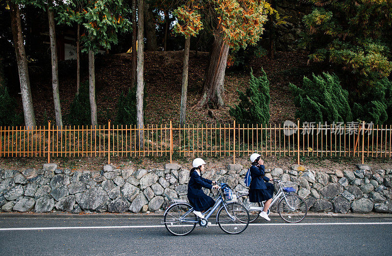 年轻的日本女孩初中学生骑自行车在和平的街道上