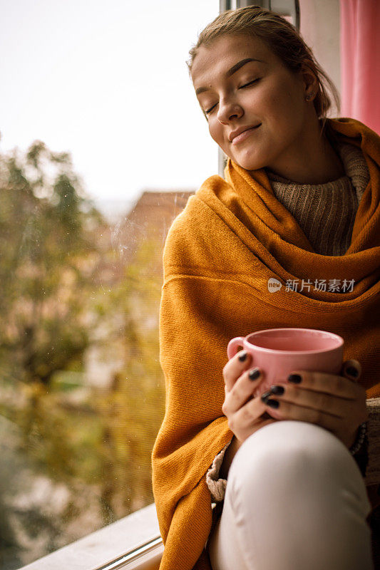 年轻女子享受着寒冷的秋日，在一杯茶上暖手