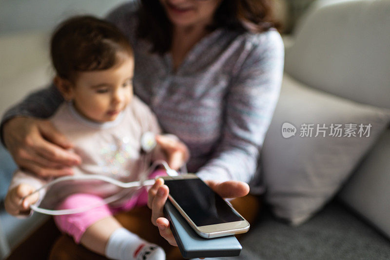 特写的妇女与婴儿抱着智能手机的便携式充电器