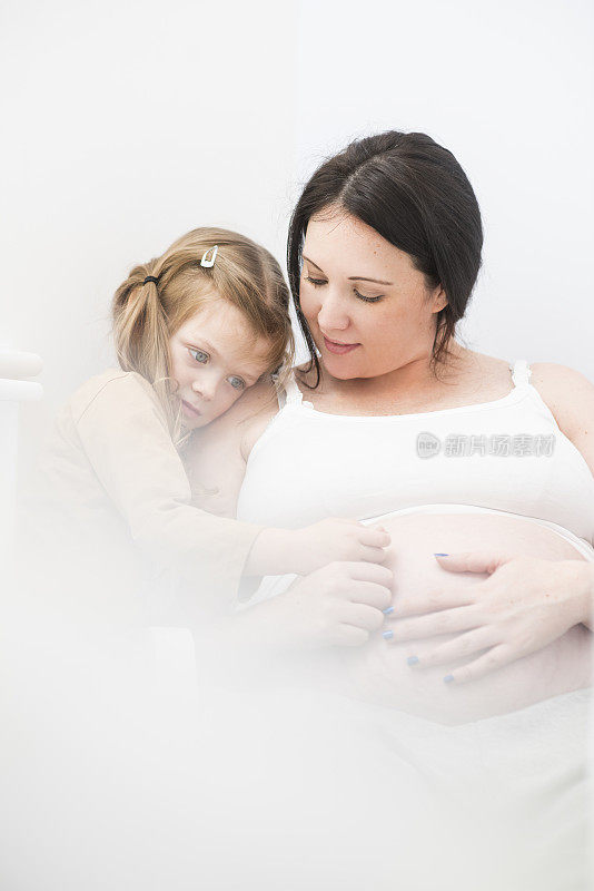 母亲和女儿拥抱在一起看着孕肚