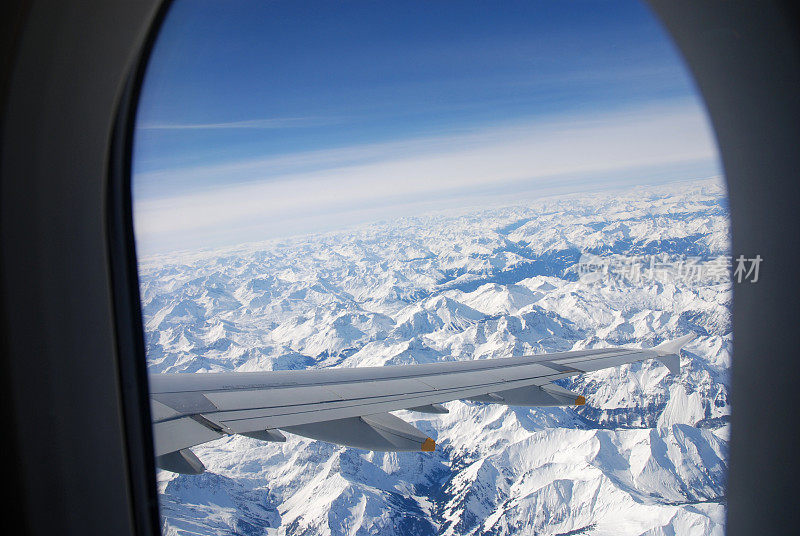 在飞机上透过窗户眺望白雪覆盖的阿尔卑斯山