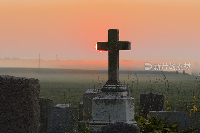 雾蒙蒙的墓地日出和大理石十字架