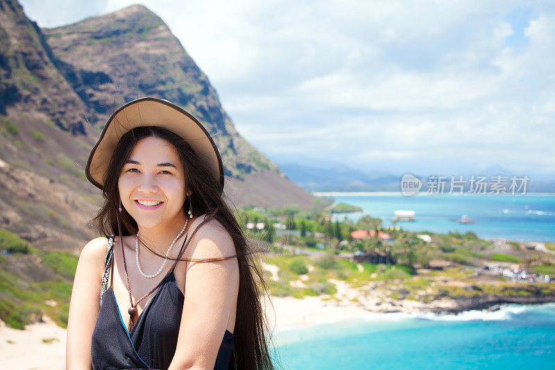 微笑的混血少女与夏威夷山和海滩的背景