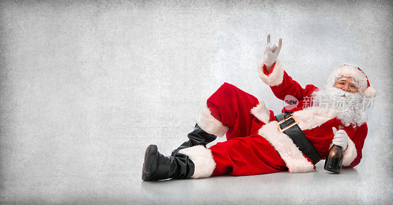 快乐的圣诞老人躺在地板上拿着一瓶酒