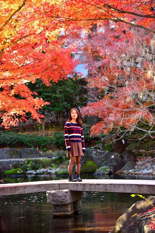 年轻的日本女子站在东京日本花园的石桥上
