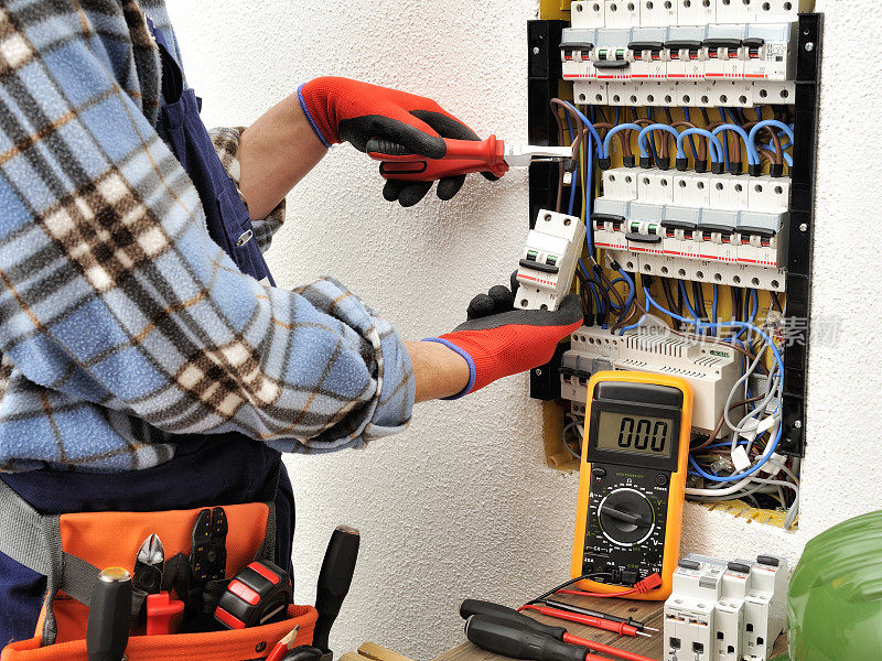 年轻的电工技术员戴着防护手套在电气面板上工作