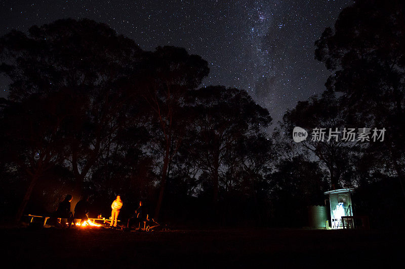 一群露营者围着篝火站着，上面闪烁着明亮的星星