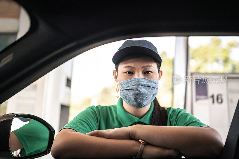 加油站服务员在加油站与顾客在汽车上交谈-带着口罩