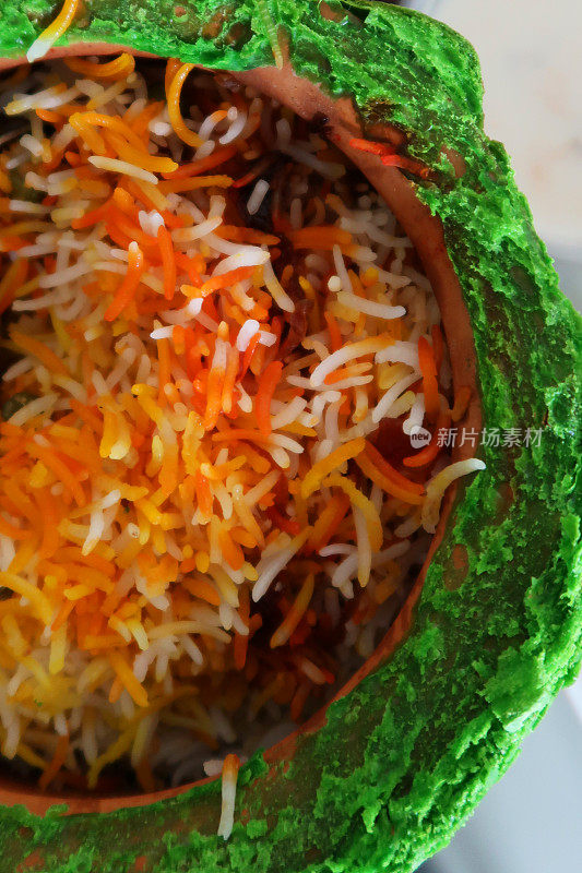 近距离的图像赤陶罐包含印度带走的米饭，鸡肉biryani与鸡肉香料酱汁在玻璃桌上，俯瞰