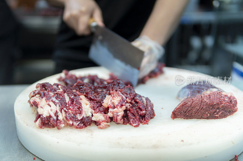 在一家牛肉火锅餐厅的开放式厨房里，厨师正在用刀切牛肉