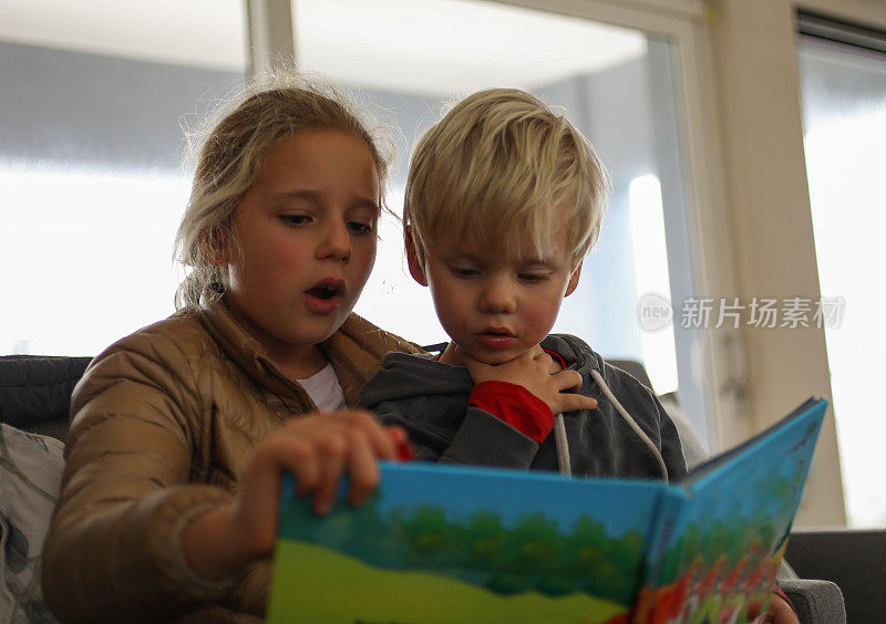 一个小女孩给一个小男孩读故事书。