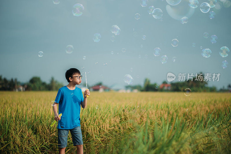 亚洲华人微笑男孩享受和玩泡泡棒在稻田