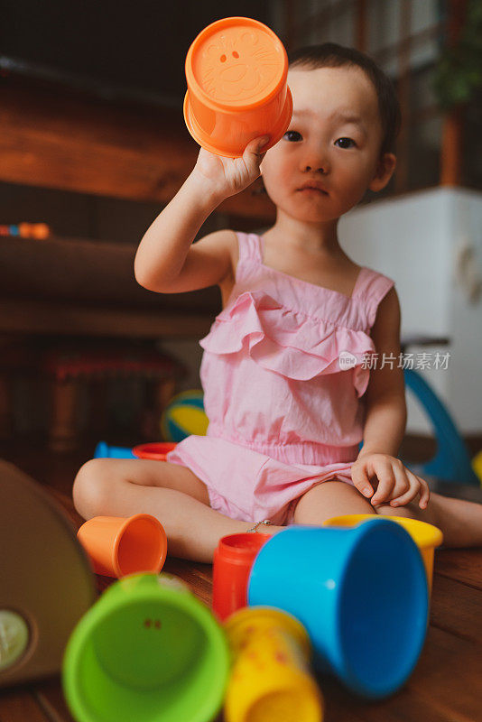 一个富有表现力的亚洲蹒跚学步的孩子在家里玩五颜六色的堆叠杯子