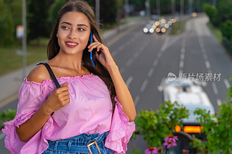 年轻美丽的女孩使用她的智能手机在繁忙的城市街道晚上