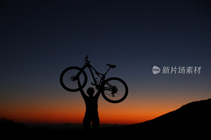 日出时，一个骑自行车的人把自行车举过头顶的剪影。