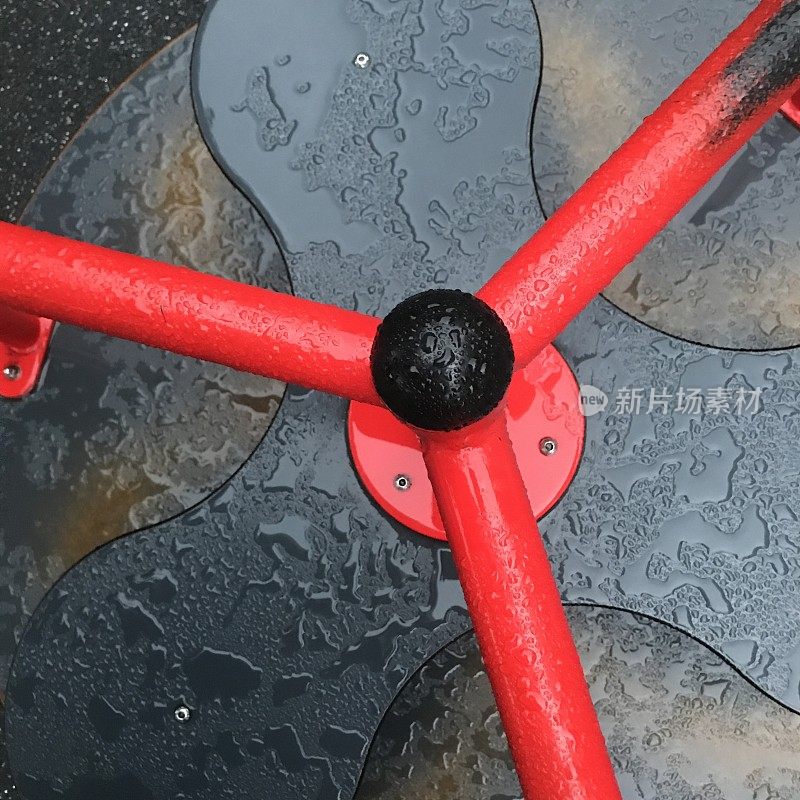 红色和黑色的旋转木马在公共操场上被雨淋湿