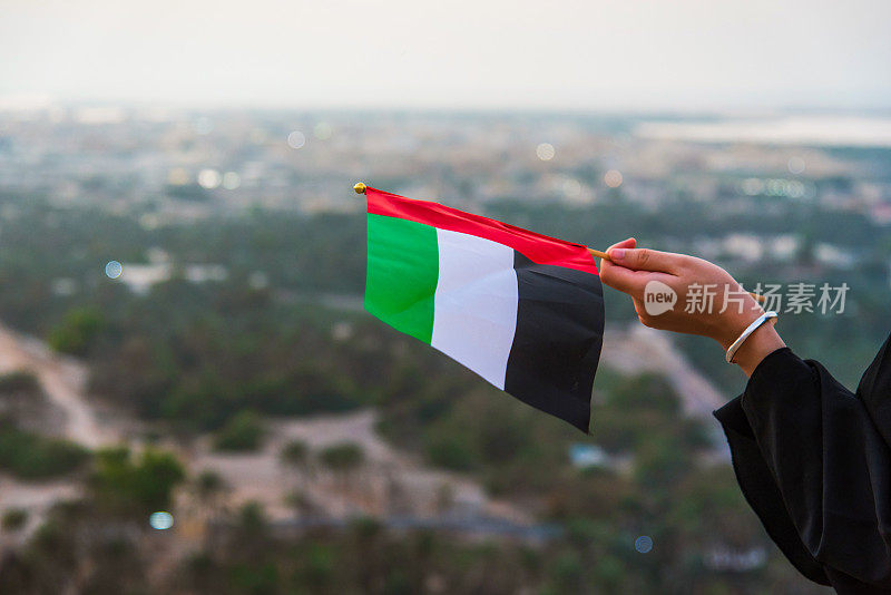日落时分，一名阿联酋妇女在沙漠山区中手持阿联酋国旗