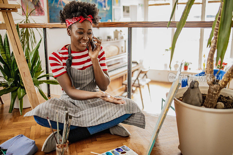 年轻的非洲裔美国妇女一边在家里画画，一边讲电话