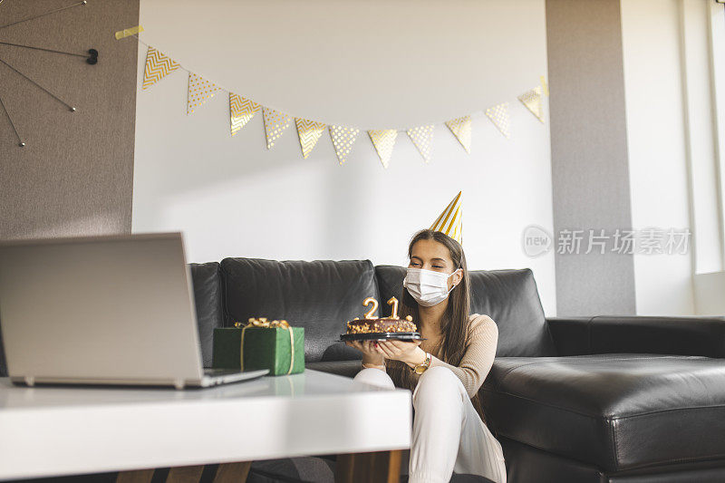 在新冠肺炎大流行期间，快乐的小女孩打开礼物，与朋友视频通话，庆祝自己的21岁生日