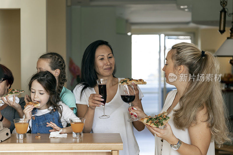 几代同堂的一家人围坐在餐桌上吃美味的披萨。全家举杯共饮。