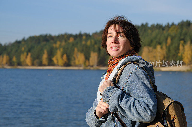 成熟的女人在阳光明媚的秋天自然公园的湖岸