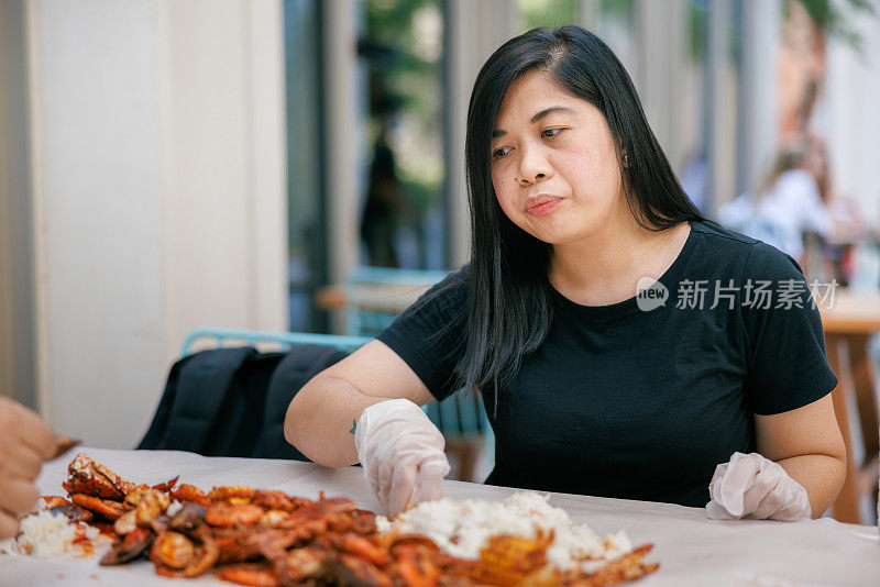 妇女坐在餐桌旁，戴着保护手套，吃着成堆的海鲜和米饭