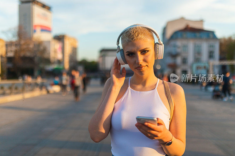 美丽的年轻女子，金色短发，一边听音乐，一边穿过城市