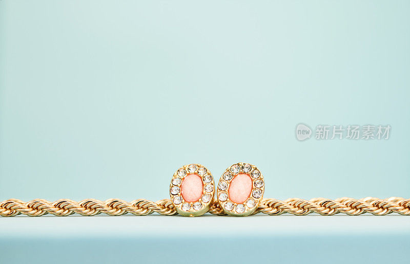 金绳链项链与粉红色宝石耳环在明亮的蓝色工作室设置与复制空间