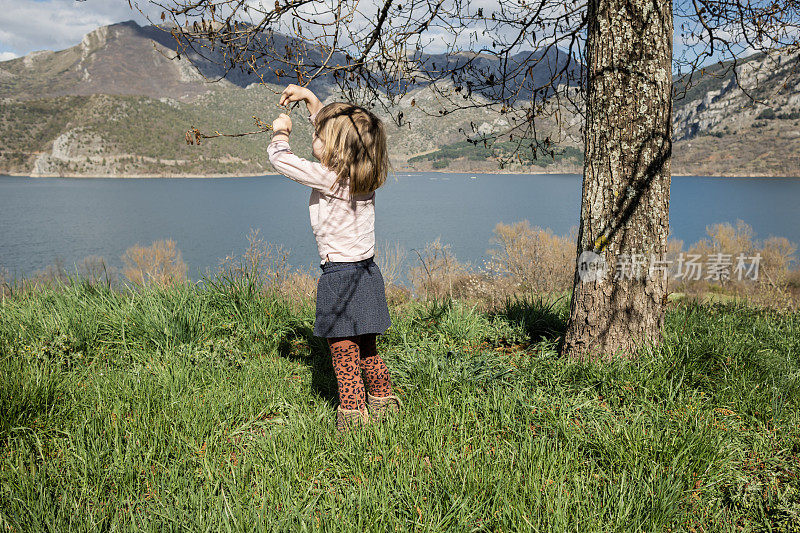 一个小女孩在湖边抓一只树枝上的昆虫。
