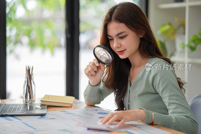 一个女人用放大镜看报告中的数字，然后用计算器计算。